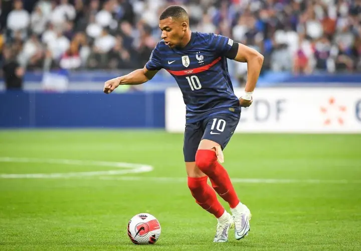 Kylian Mbappé w niebieskiej koszulce z numerem 10, w czerwonych getrach, wykonuje najszybszy sprint w piłce nożnej, prowadząc piłkę.