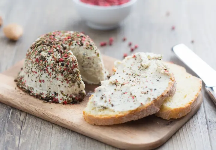 Queso vegano cubierto de pimienta y hierbas, servido en rebanadas de pan rústico.