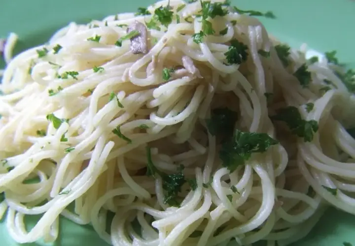 Pyszne spaghetti z anchois i natką pietruszki, podane na zielonym talerzu.