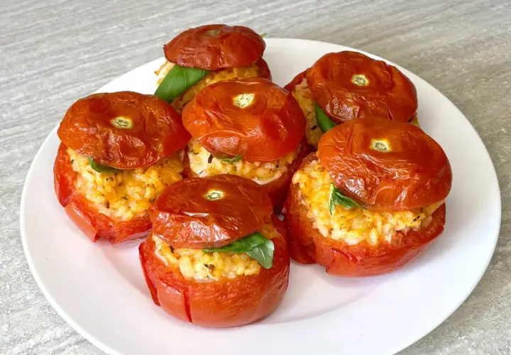 Sei pomodori ripieni di riso e basilico, cotti al forno, su un piatto bianco.