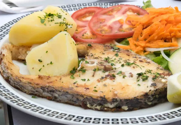 Un succulento pesce spada al forno, servito con patate bollite, pomodori a fette, carote grattugiate e insalata fresca.