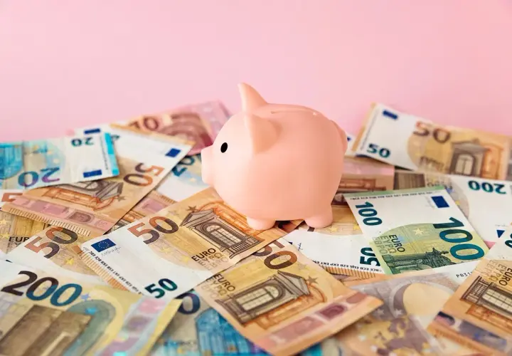 Różowa świnka-skarbonka na stosie banknotów euro. Zastanawiasz się nad oprocentowaniem konta walutowego?