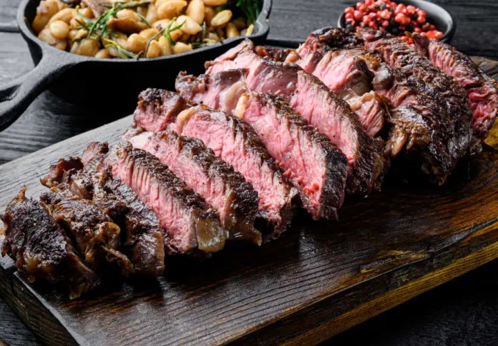 Côte de bœuf juteuse, tranchée et prête à être dégustée. Parfaitement cuite sur la plancha, accompagnée de haricots et de poivre rose.