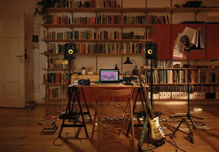 Bureau de musique avec ordinateur affichant un logiciel comme FL Studio, enceintes, guitare et microphones, entouré d'étagères remplies de livres.