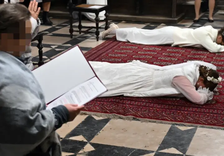 Dwie kobiety w białych sukniach leżą na dywanie w kościele. To uroczystość, podczas której zostają dziewicami konsekrowanymi.