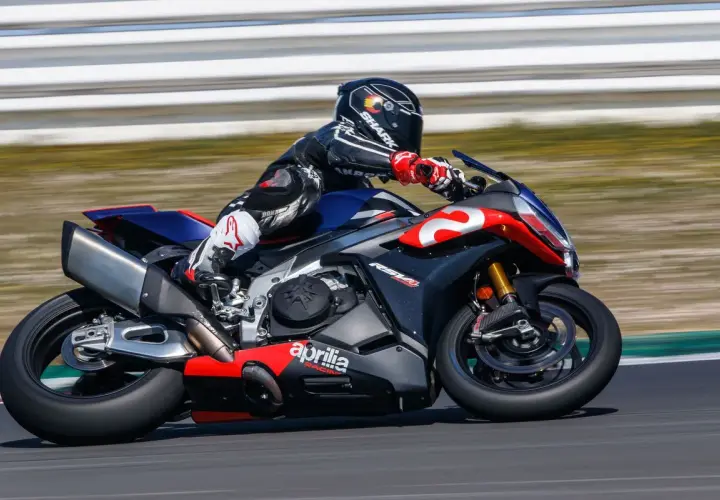 Piloto en una Aprilia RSV4 1100 en circuito, con traje de cuero negro y rojo, casco Shark.