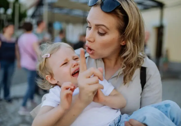 Bambina piange mentre la madre, forse afflitta da depressione, cerca di calmarla. Gli effetti della madre depressa sui figli adulti sono complessi.