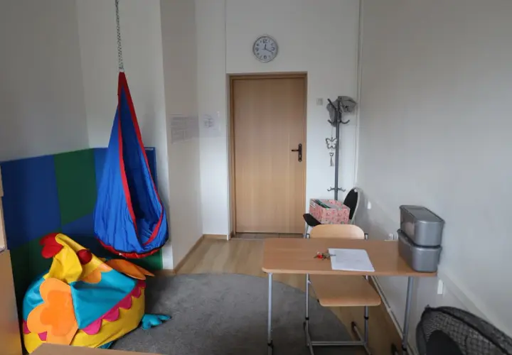 Przytulny gabinet pedagoga szkolnego z kolorowym workiem sako w kształcie ptaka, huśtawką i biurkiem.