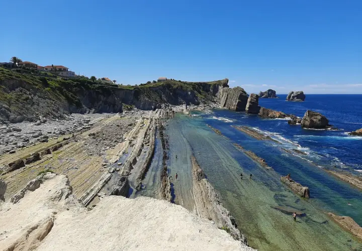 Espectacular vista de la playa de Arnia con sus formaciones rocosas y aguas cristalinas. Personas disfrutan del mar.