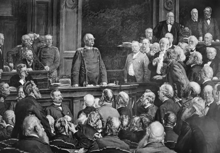 Bismarck steht im Mittelpunkt einer Versammlung, die den Berliner Vertrag darstellt. Männer in Anzügen und Uniformen diskutieren.