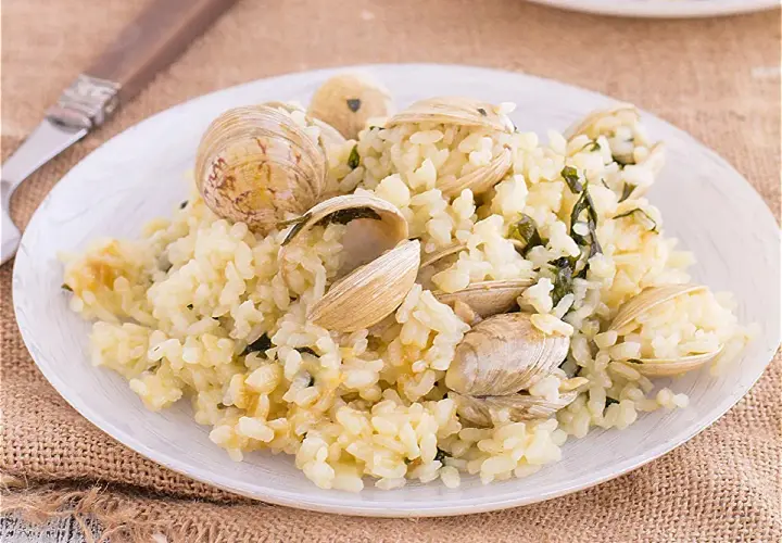 Un plato de arroz cremoso con almejas frescas, adornado con hierbas verdes. Un delicioso arroz con almejas listo para disfrutar.