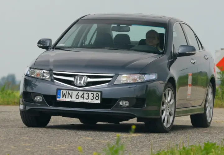 Ciemnoszary Honda Accord z kobietą za kierownicą jedzie po drodze.