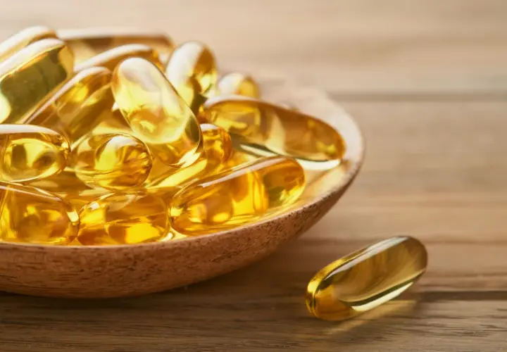 Goldene Kapseln auf einem Holzlöffel, die die positive Wirkung von Omega-3 auf die Psyche symbolisieren.