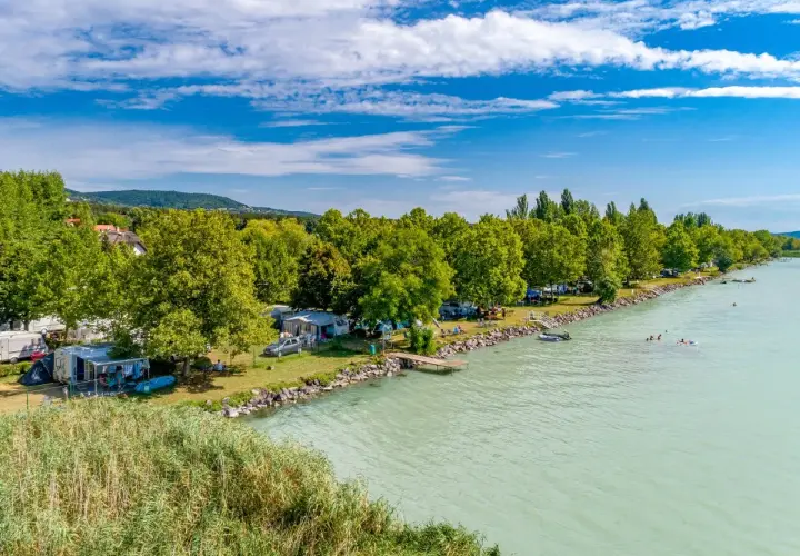 Słoneczny dzień na kempingu Balaton. Przyczepy kempingowe i namioty nad turkusową wodą, ludzie pływają i relaksują się.