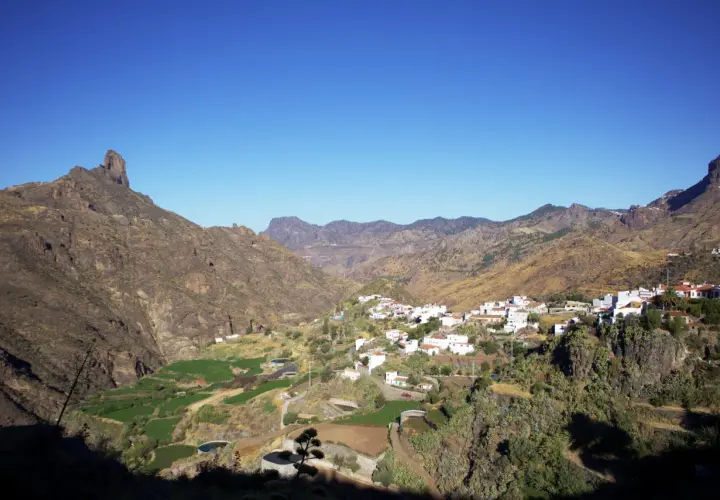 Pueblo blanco de Tejeda, Gran Canaria, con montañas escarpadas y campos verdes en un día soleado.