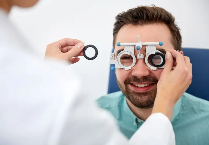 Badanie wzroku u optometrysty. Mężczyzna z uśmiechem na twarzy, któremu zakładane są soczewki próbne. To pierwszy krok, by dowiedzieć się, jak zostać optometrystą.