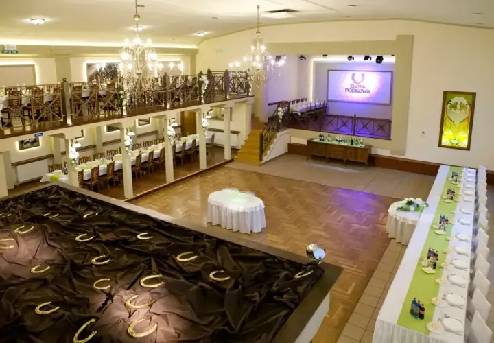 Elegancka sala weselna z podkowami na ciemnym materiale, stołami i ekranem z logo "Złota Podkowa".