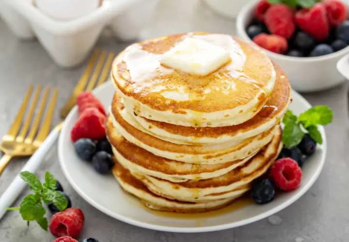 Pile de pancakes sans oeuf, dorés et moelleux, garnis de beurre fondant et de fruits rouges frais. Un délice pour le petit-déjeuner !
