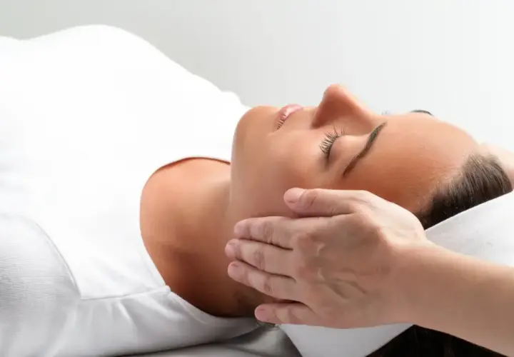 Kobieta w białej koszulce doświadcza relaksującego dotyku dłoni. To może być właśnie reiki co to za technika, która przynosi ukojenie.