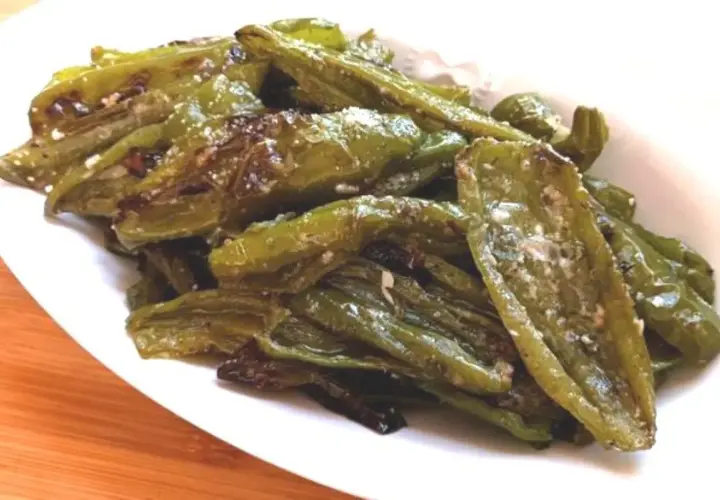 Friggitelli al forno, verdi e lucidi, conditi con sale e spezie, serviti su un piatto bianco.