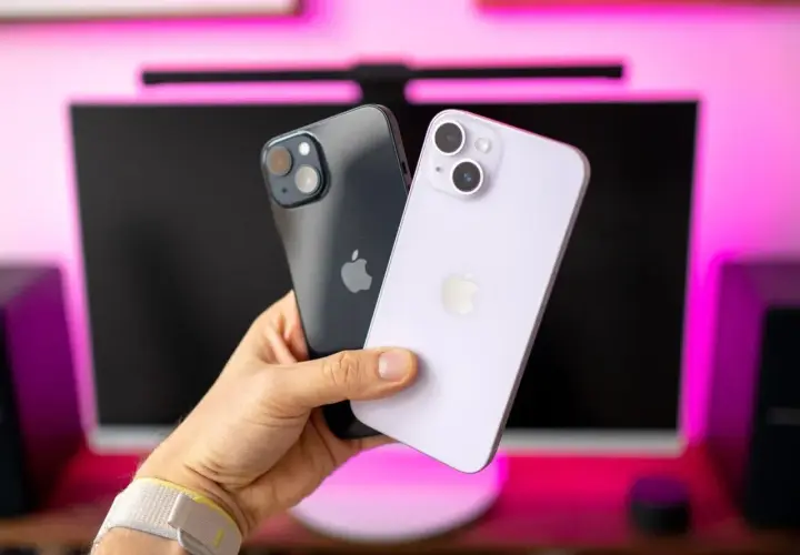 Dwa iPhone'y 14 w ręce, jeden ciemny, drugi fioletowy. Ich aparat jest gotowy do robienia zdjęć.