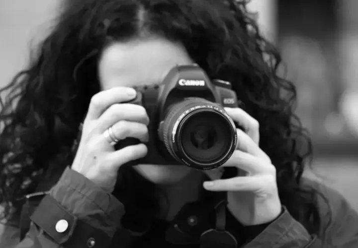 Kobieta z kręconymi włosami robi zdjęcie aparatem Canon. To jej pierwszy kurs na fotografa, uczy się łapać kadr.
