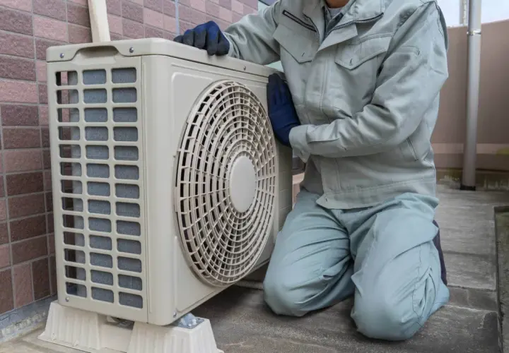Pracownik w rękawiczkach sprawdza jednostkę zewnętrzną klimatyzacji. Wzór pozwolenia na montaż klimatyzacji w bloku jest kluczowy dla takich prac.