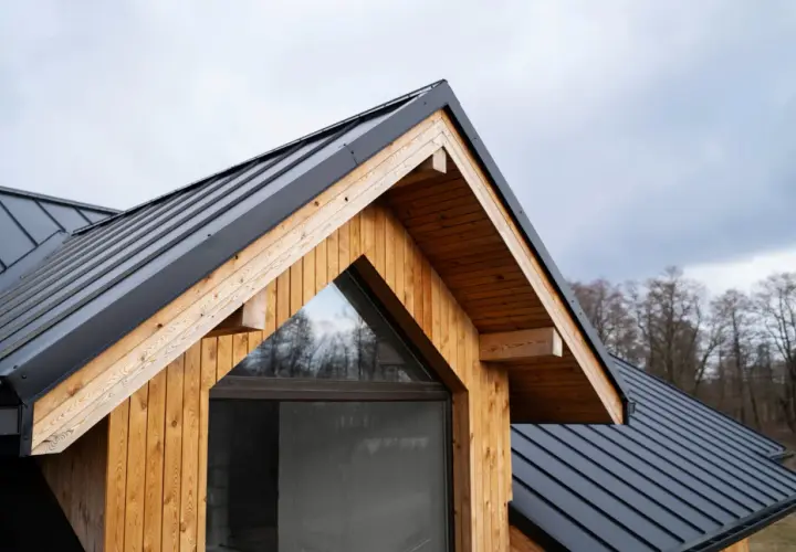 Tetto spiovente in metallo nero e legno naturale, con una finestra triangolare. Il legno, trattato per resistere agli agenti atmosferici, mostra il suo **impregnato significato** di protezione e calore.