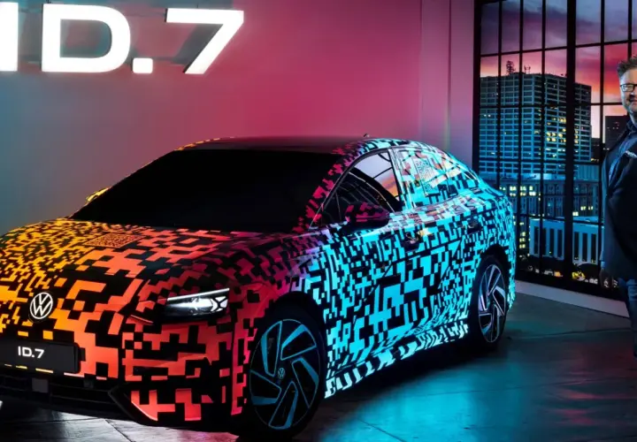 Nowy Volkswagen ID.7 prezentuje się w neonowym blasku, z efektownym wzorem QR kodu na karoserii. Obok stoi mężczyzna w garniturze, a w tle widać nocną panoramę miasta.