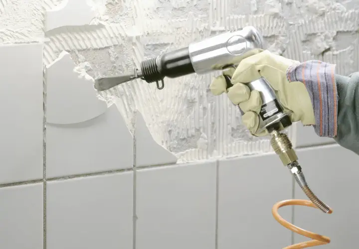 Mit einem Pressluftmeißel wird alter Fliesenkleber von der Wand entfernt.