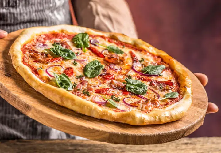 Pyszna pizza z rukolą i cebulą na drewnianej desce. Czy pizza jest lekkostrawna? Ta wygląda apetycznie!