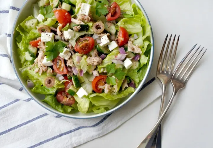Insalata fresca con lattuga, pomodorini, cetrioli, olive, cipolla rossa, cubetti di feta e tonno sminuzzato.