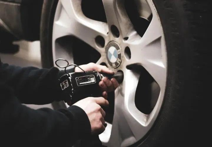 Mano usando una llave de impacto para cambiar ruedas delanteras por traseras en un coche BMW.