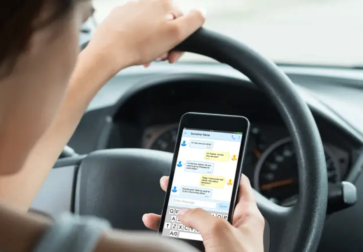 Person håller en telefon i bilen och skriver ett meddelande.