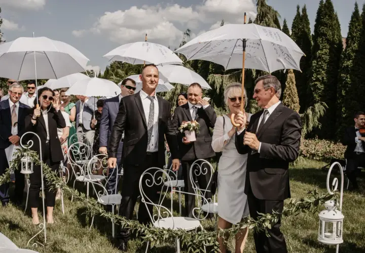 Wesele w kwietniu pod białymi parasolami. Goście w eleganckich strojach czekają na ceremonię na trawie, wśród zieleni i ozdobnych krzeseł.