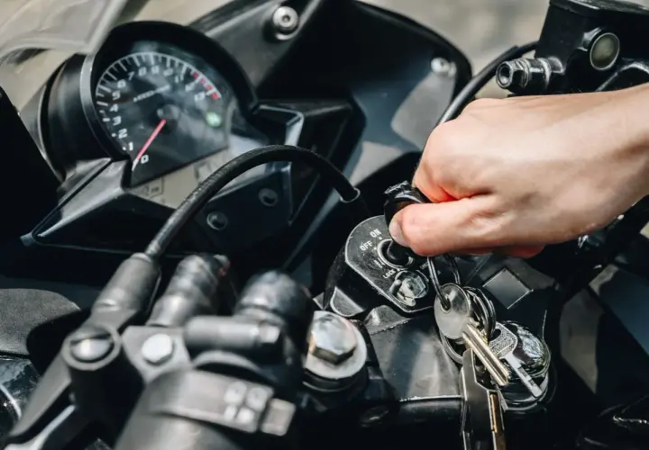 Mano girando la llave de contacto de una moto, pero no enciende. El tablero y las llaves están visibles.