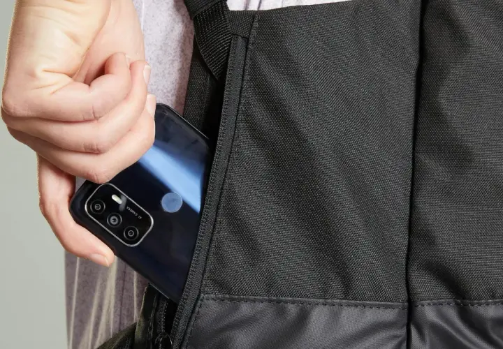 Dłoń wkłada telefon do bocznej kieszeni czarnego plecaka. Idealny, jaki plecak na rower, by mieć wszystko pod ręką.
