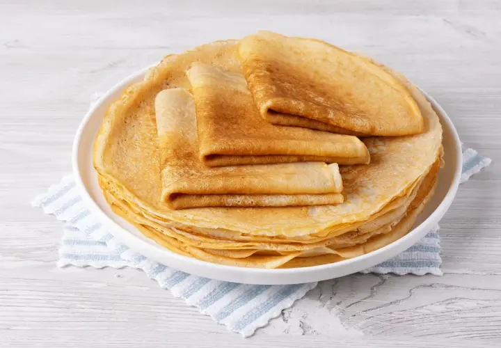 Pile de crêpes dorées, certaines pliées, sur une assiette blanche. Un délice sans oeuf pour un petit-déjeuner léger.