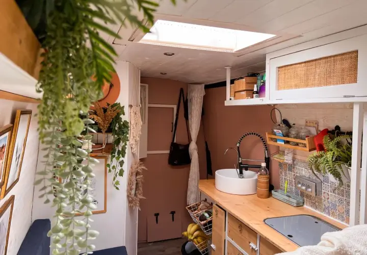Intérieur de fourgon aménagé : cuisine avec évier, robinet, placards et plantes.