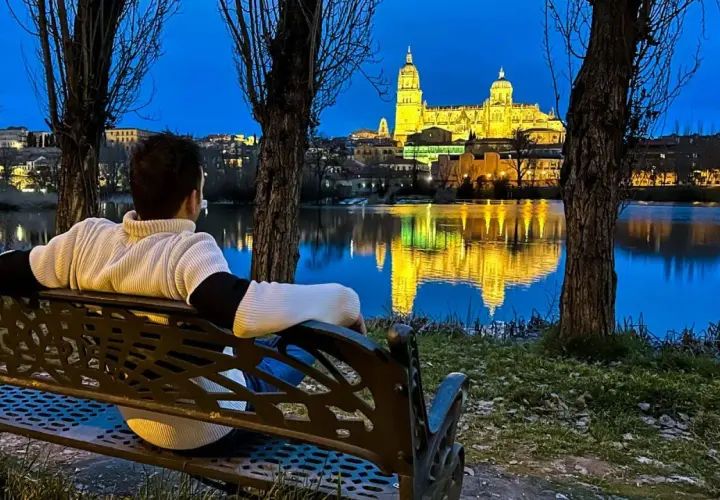 Persona sentada en un banco contempla la Catedral de Salamanca iluminada al anochecer, reflejada en el río. Ideal para saber qué ver en Salamanca en un día.