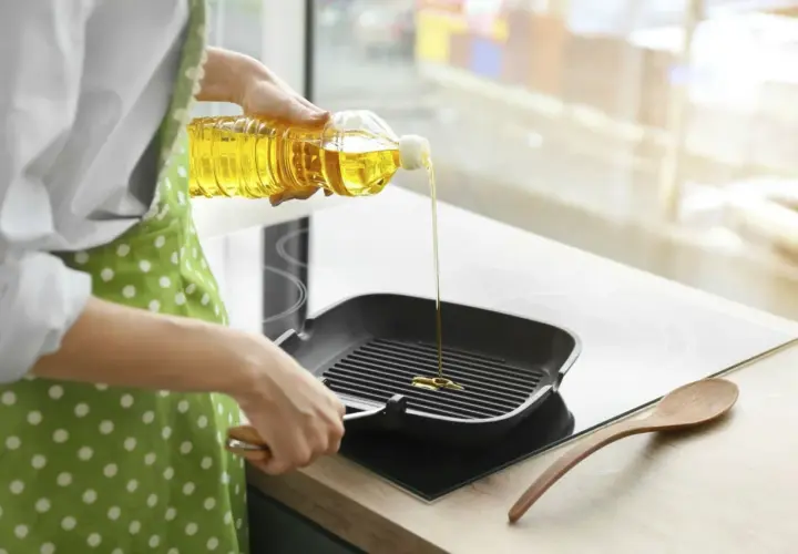 En person häller vegetabilisk olja i en grillpanna.