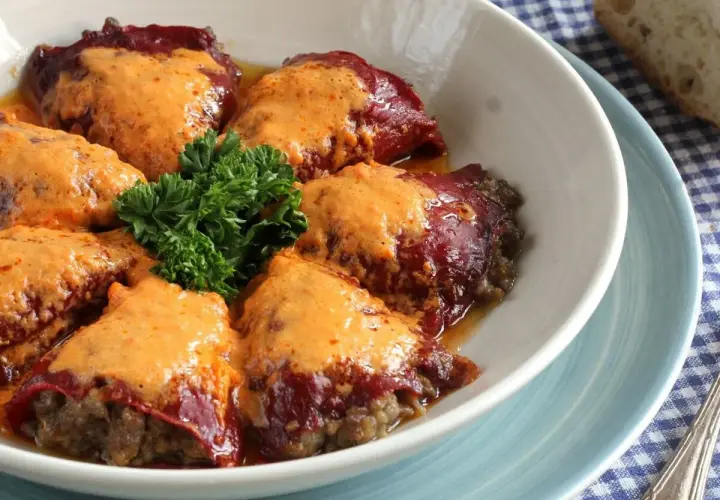 Pimientos rellenos de carne, cubiertos con una cremosa salsa naranja y adornados con perejil fresco.