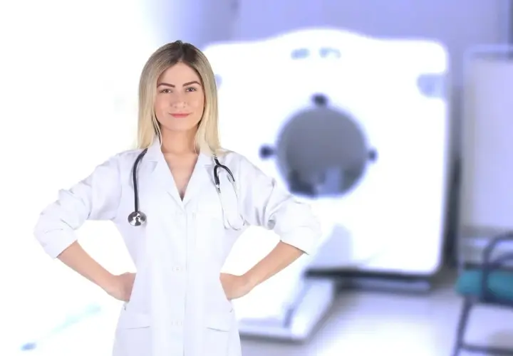 Uśmiechnięta rejestratorka medyczna w białym kitlu ze stetoskopem, na tle aparatu RTG. Zastanawiasz się, ile zarabia rejestratorka medyczna?