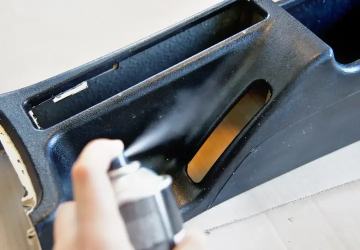 Ręka trzyma puszkę z farbą w sprayu, wykonując malowanie plastików. Odświeżanie wnętrza samochodu.