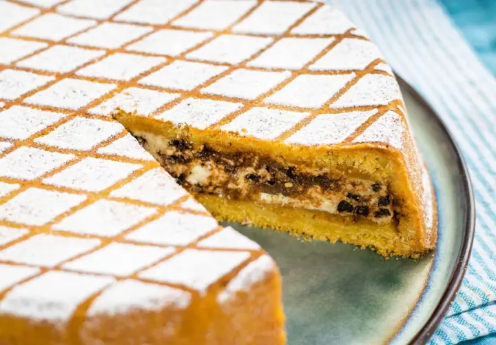 Una fetta di cassata al forno, con la sua copertura a rombi di zucchero a velo, rivela un ripieno goloso di ricotta e cioccolato.