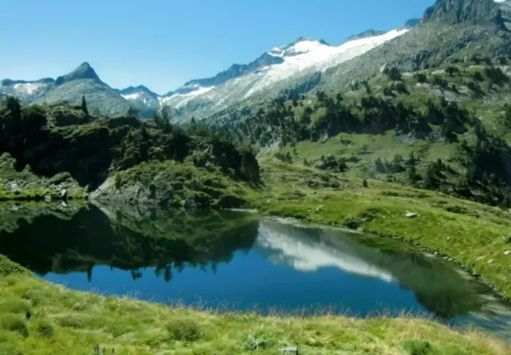 Reflejo de montañas nevadas en los ibones de Villamuerta, un paisaje alpino sereno.