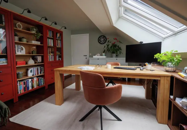 Accogliente angolo studio in mansarda con scrivania in legno, librerie rosse e lucernario.