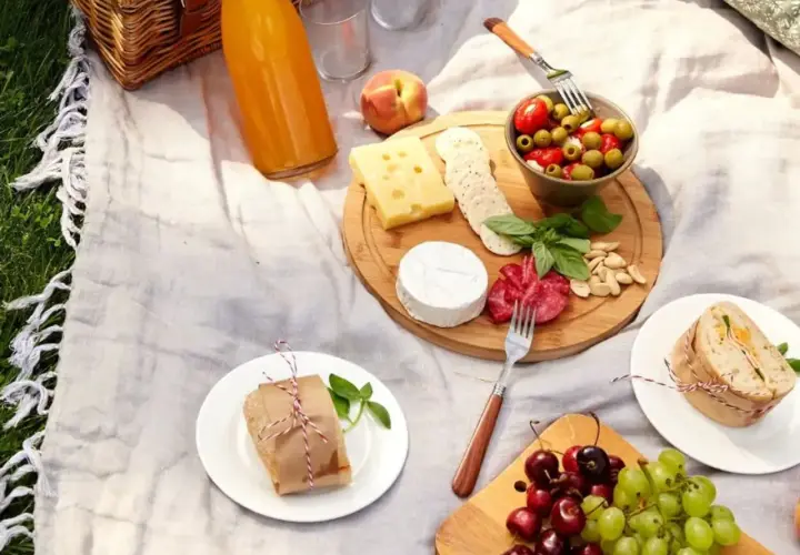 Idée de que prendre pour un picnic entre amis : plateau de fromages, charcuterie, olives, fruits, sandwichs et jus.