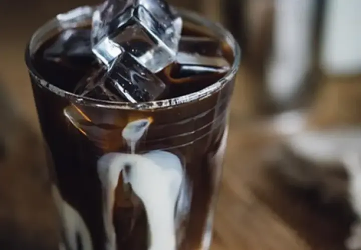 Ett glas med is och mörk, stark kaffe där grädde virvlar ner. En perfekt vietnamesisk iskaffe för en varm dag.