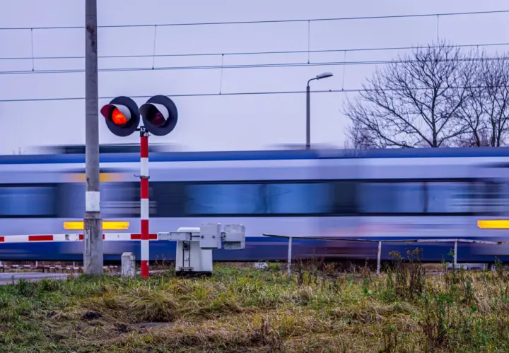 Pędzący pociąg mija przejazd kolejowy z czerwonymi światłami, zgodnie z nowym rozporządzeniem o przejazdach kolejowych.